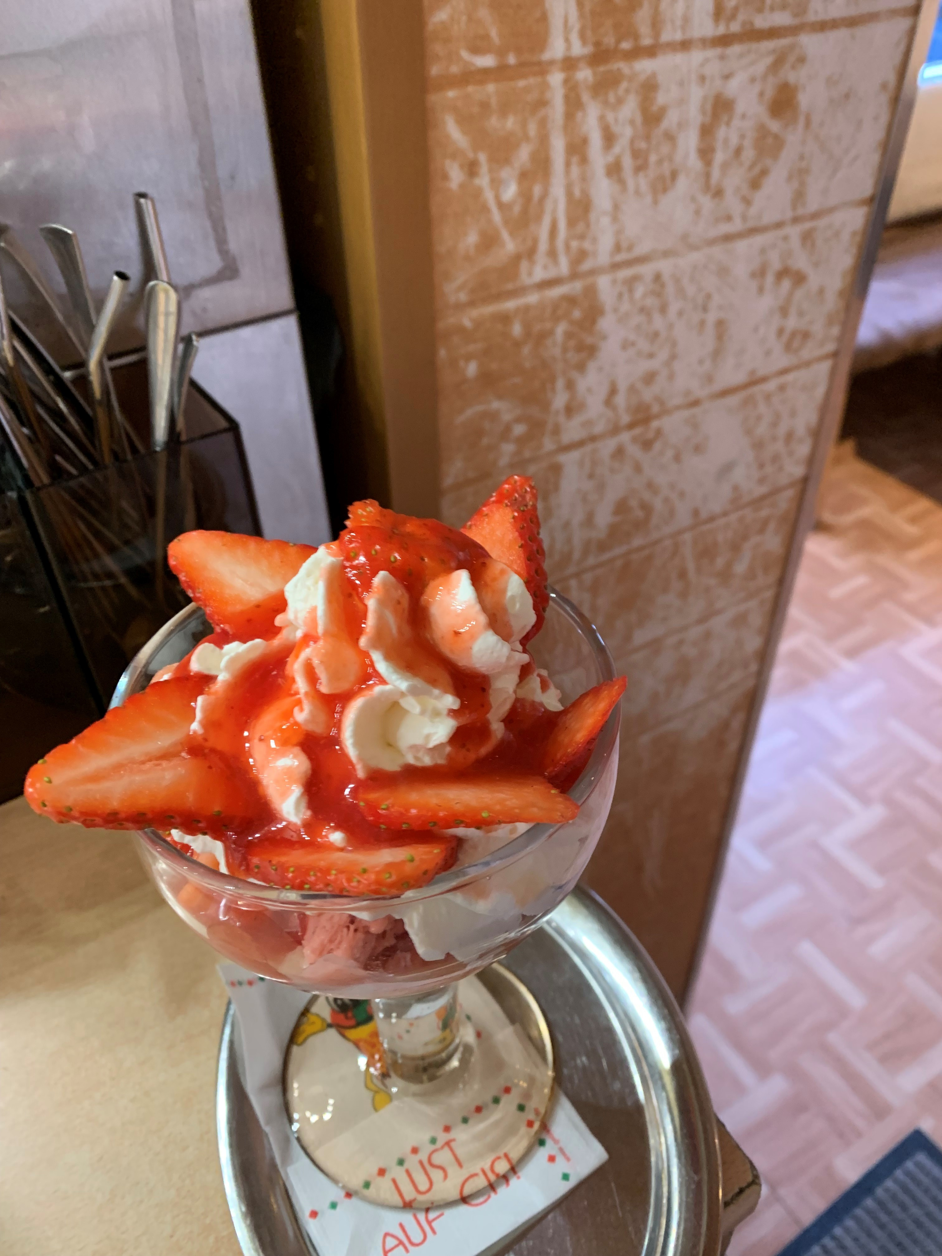 Erdbeer-Eisbecher mit reifen, frisch geschnittenen Erdbeeren und rotem Sirup, gekrönt mit Schlagsahne, serviert auf einer Café-Theke.
