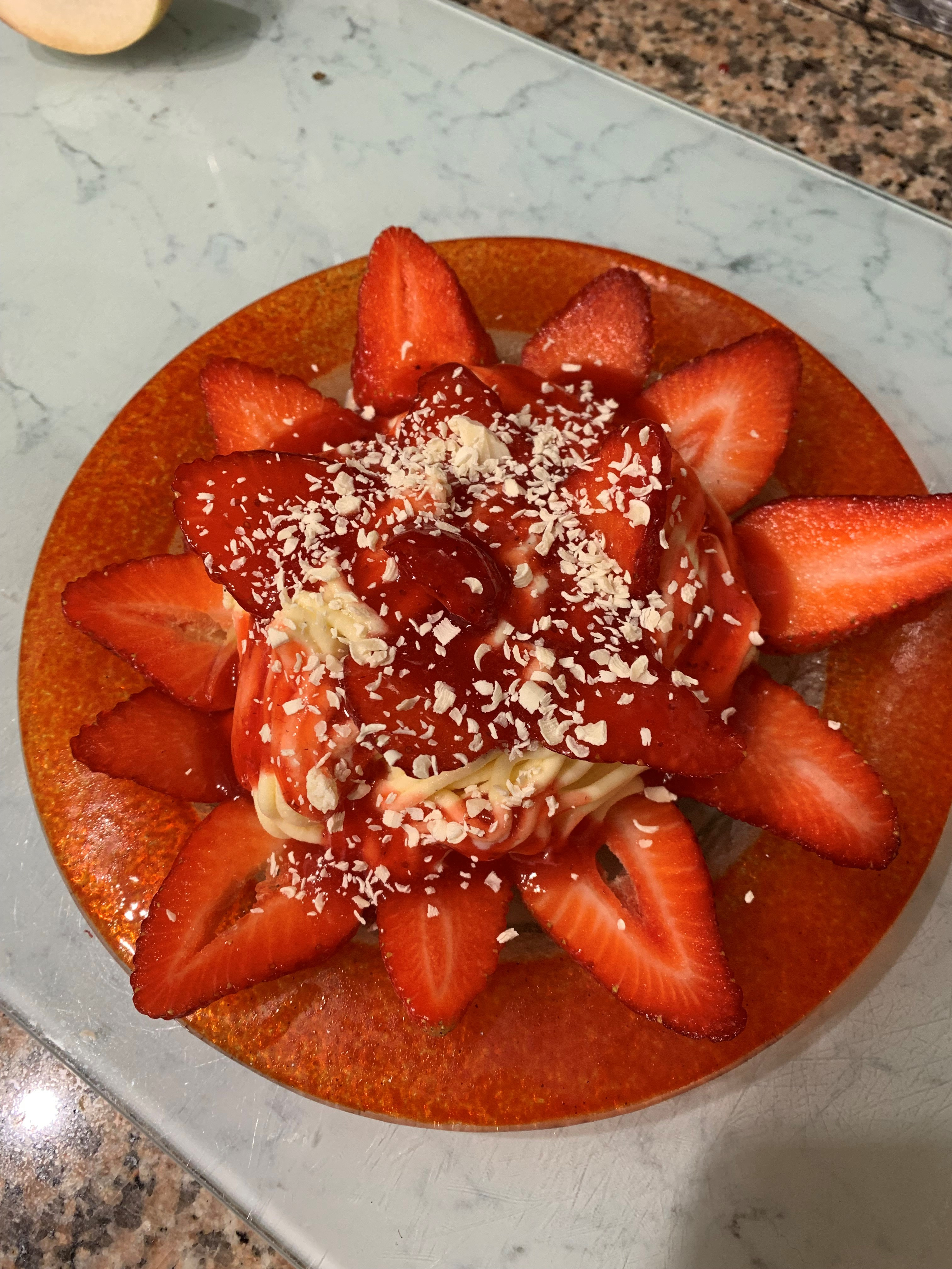 Waffel mit frischen Erdbeeren und einer großzügigen Portion Schlagsahne, beträufelt mit Erdbeersirup und bestreut mit weißen Schokoladenraspeln, präsentiert auf einem marmorierten Tresen.